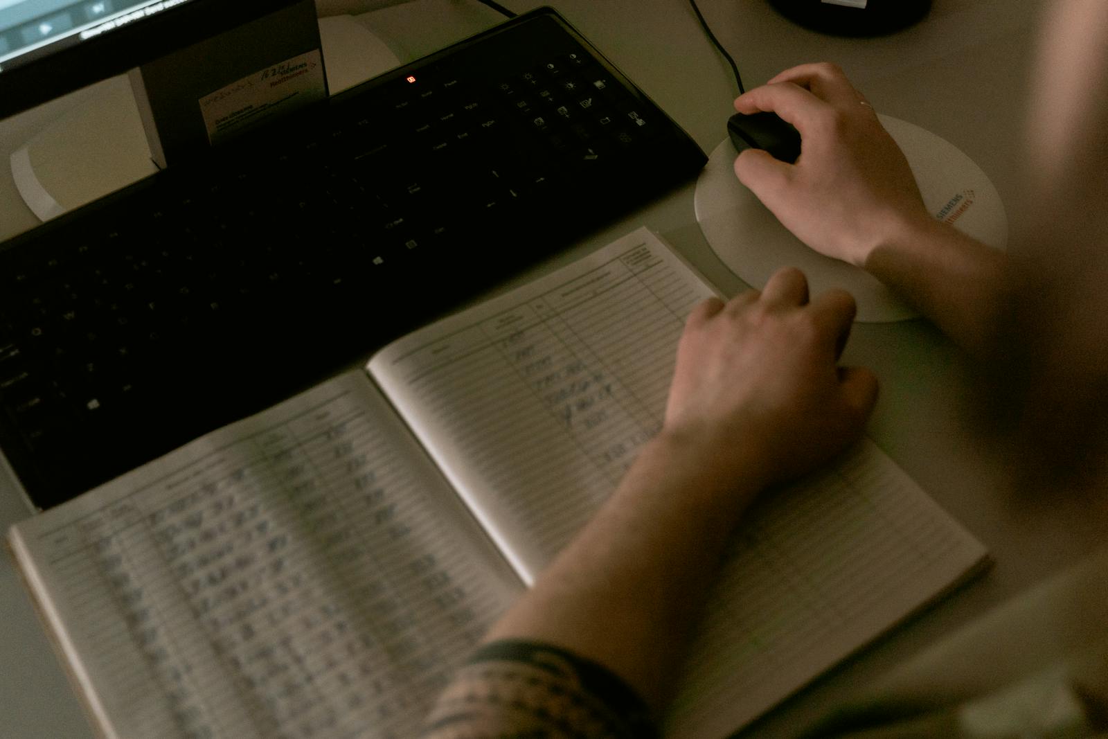 A clinical worker reviewing paper notes next to a computer.